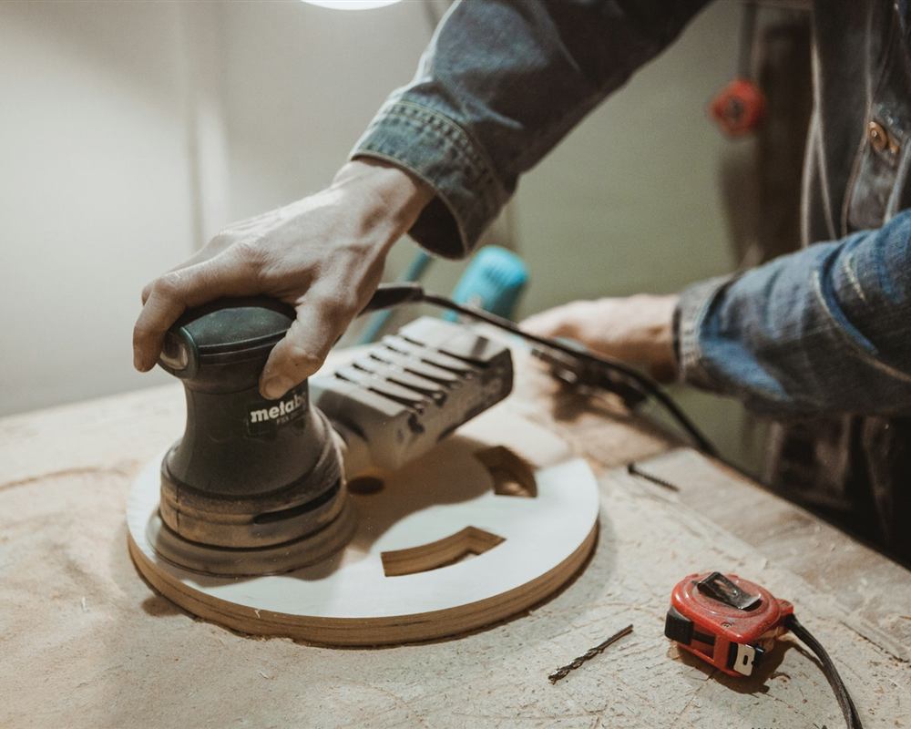 Vakman schuurt een houten werkstuk met een excentrische schuurmachine